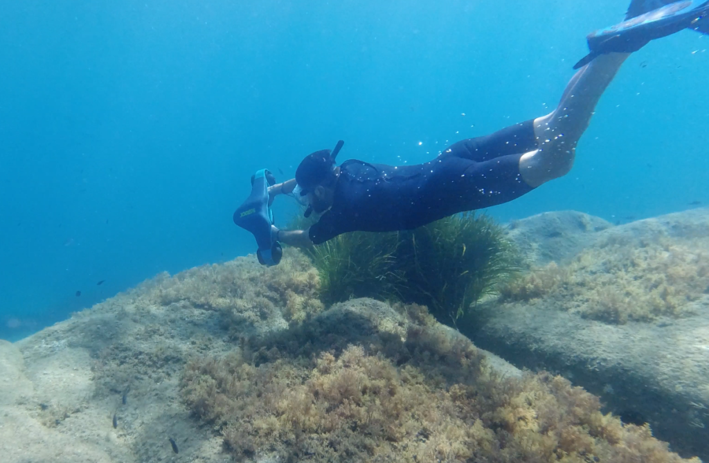 An underwater diver walking with an underwater scooter from our partner Splura